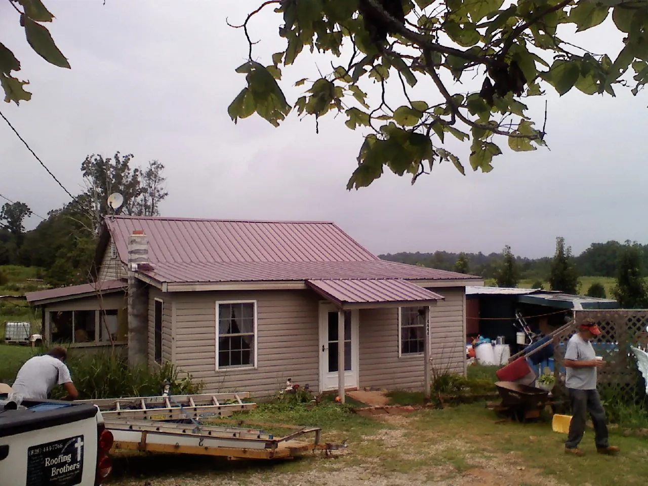 Crew finishing a mauve metal roof on a small farmhouse in Dana