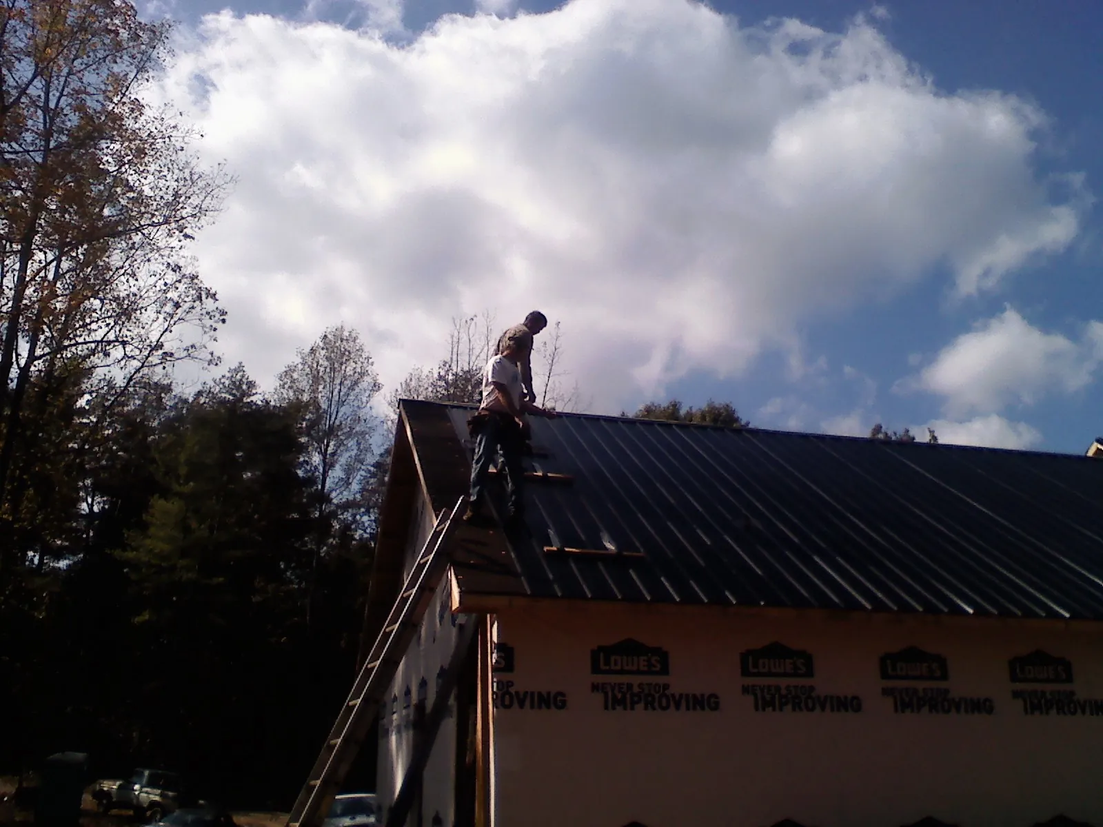 Roofer fastening dark metal panels high against a cloudy sky, from a Roof Inspection job in Dana