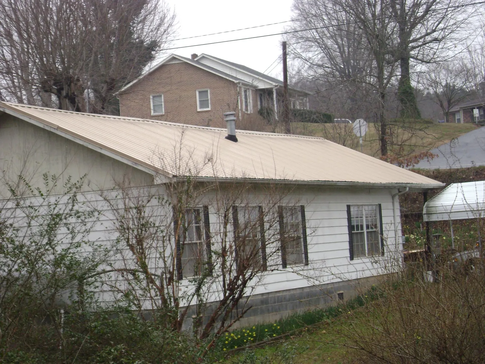 Tan metal roof on a white sided house set into a hillside — Commercial Roofing by Roofing Brothers in Dana